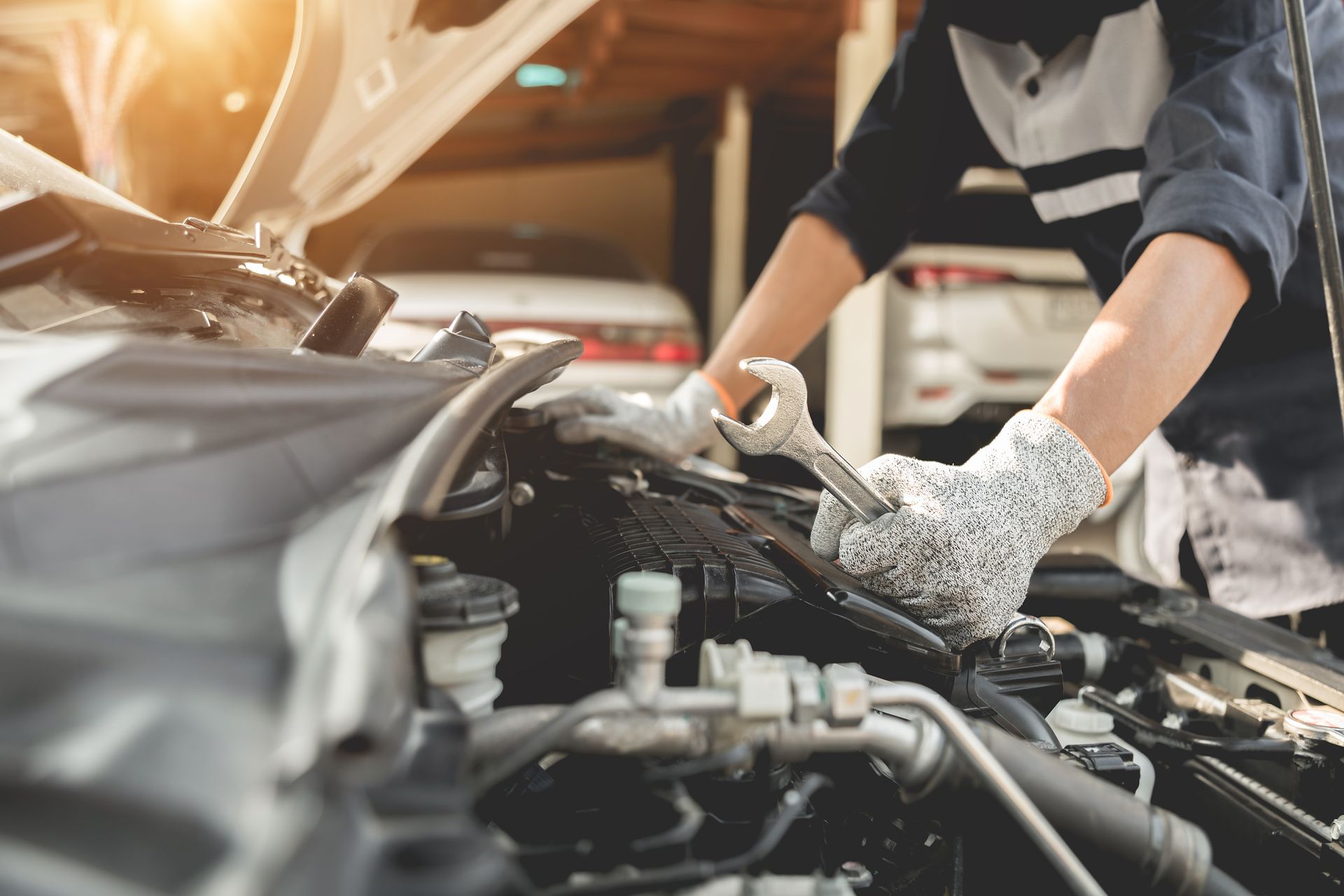A person in work gloves uses a wrench to repair a car engine in a garage.