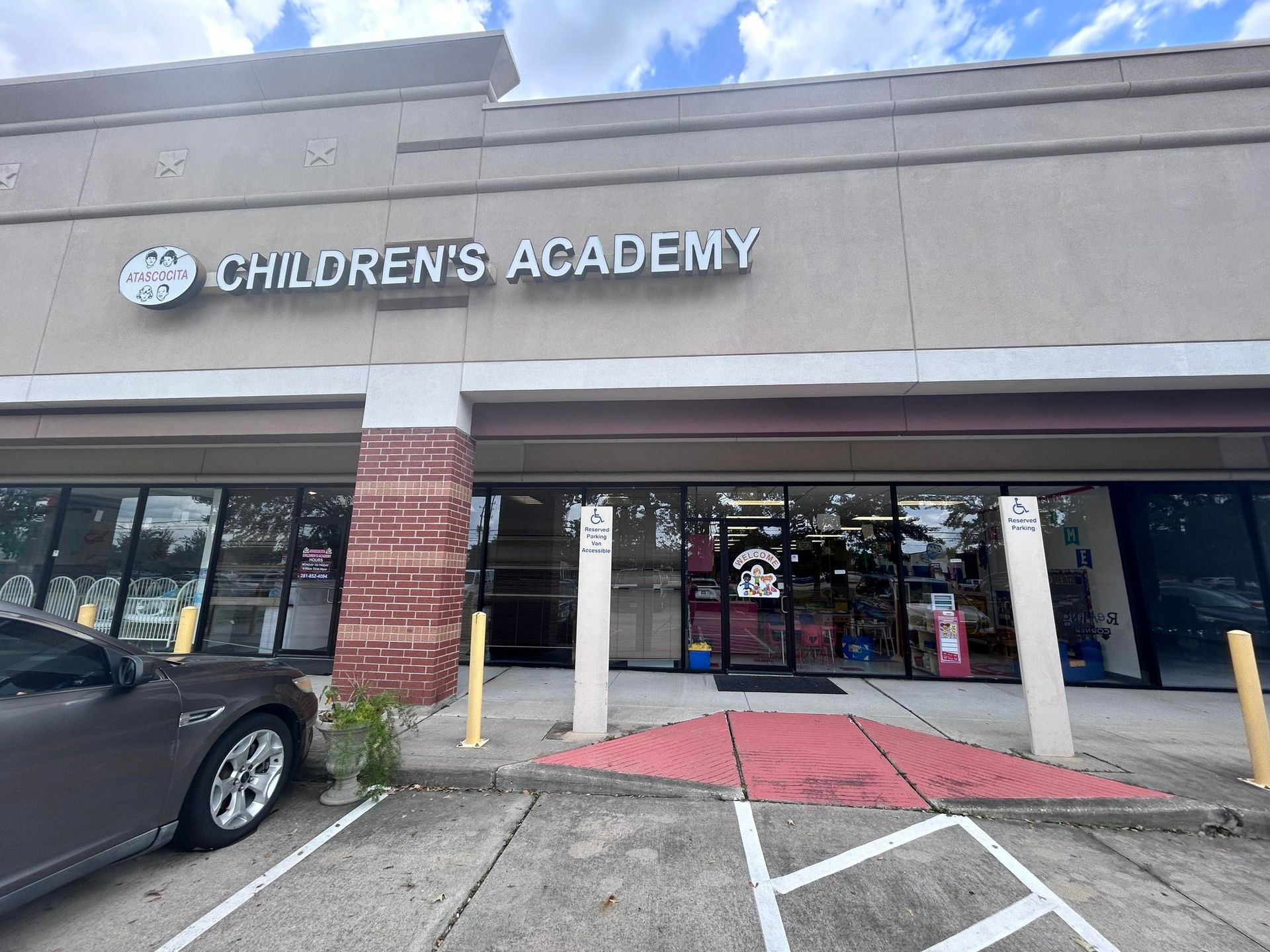 A car is parked in front of a children 's academy building.