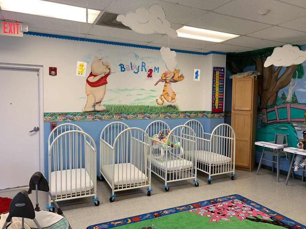 A room with cribs and a painting of winnie the pooh on the wall