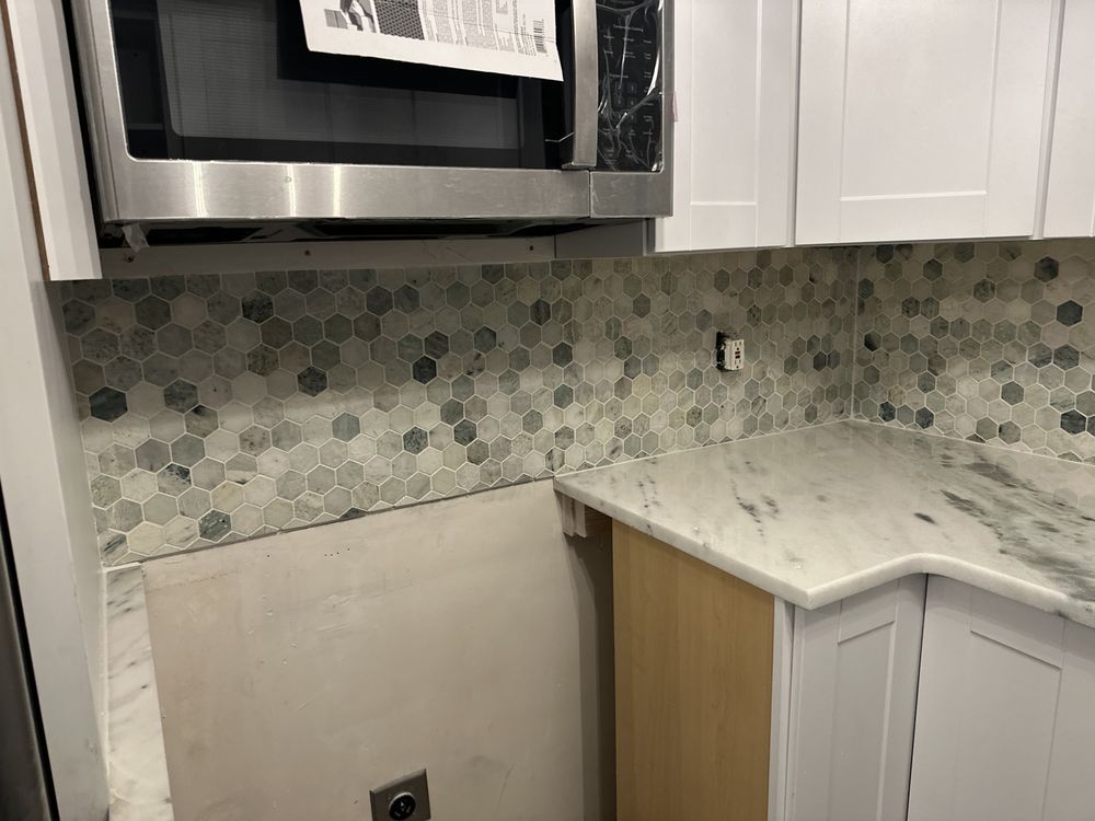 A kitchen with stainless steel appliances , white cabinets , and marble counter tops.