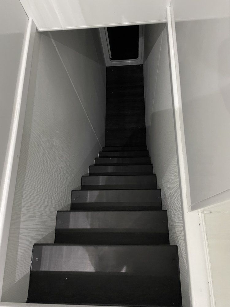 A set of black stairs leading up to a dark room.