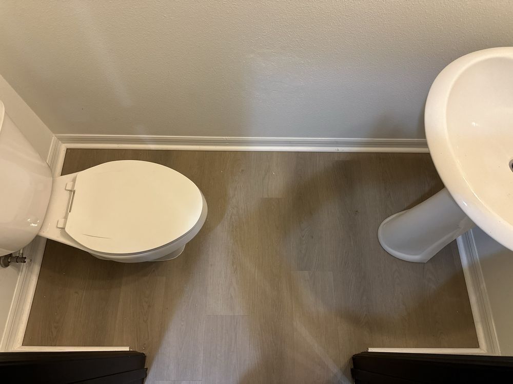 A bathroom with a toilet , sink and wooden floor.