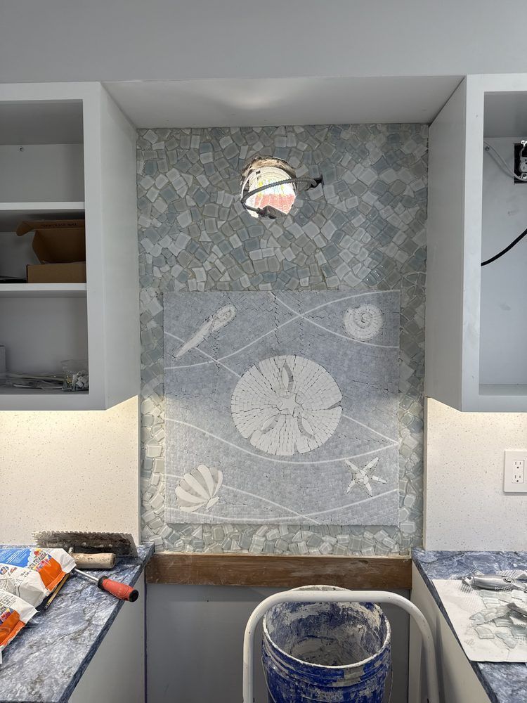 A kitchen with a sand dollar on the wall and a bucket of paint on the counter.