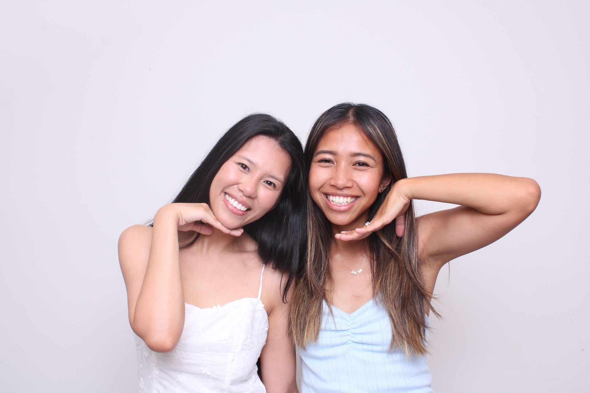 Photo Booth first birthday. Two smiling people with arms raised, creating frames around their faces, standing in front of a white backdrop.