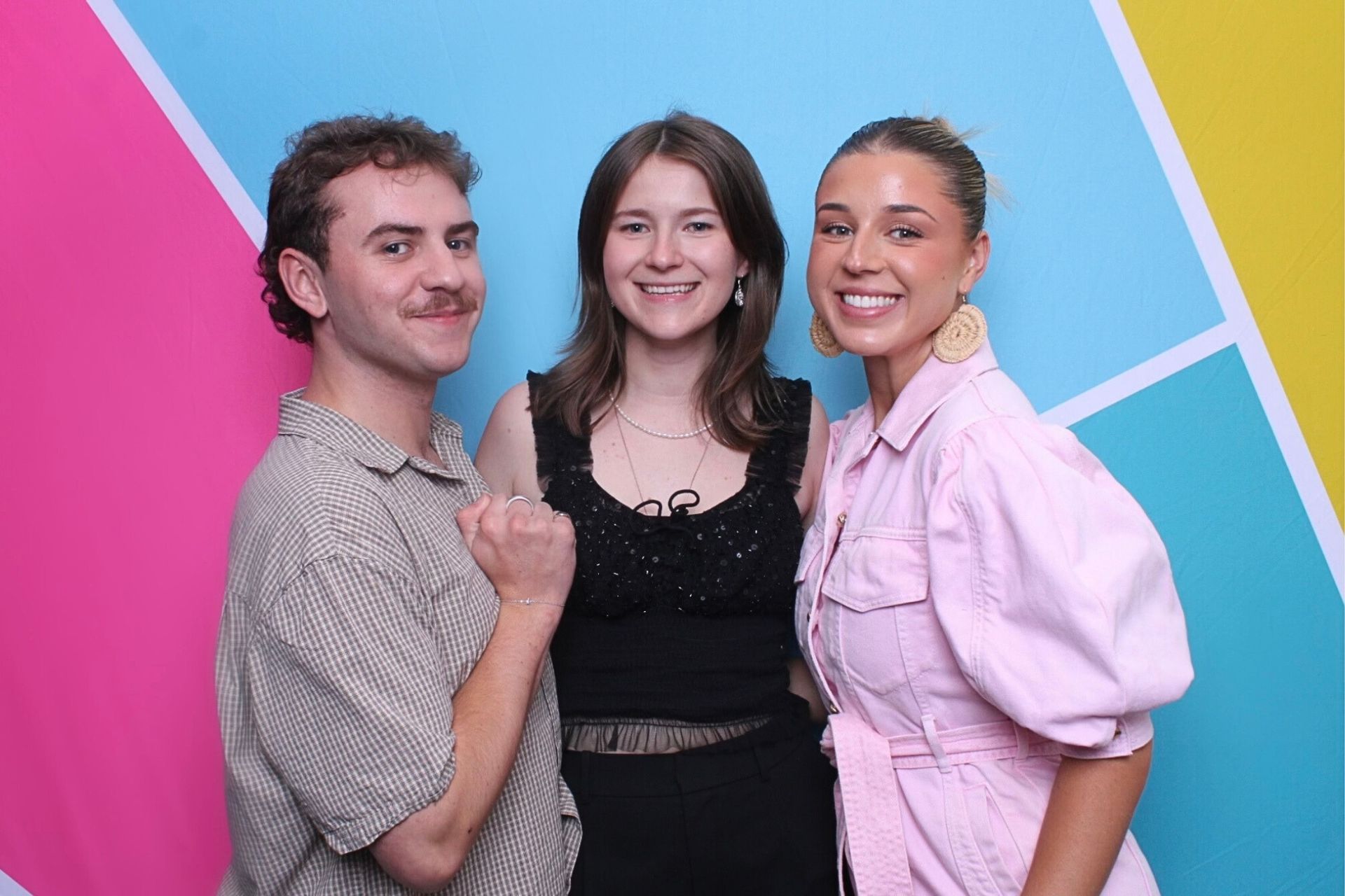 Three people posing in front of a colorful backdrop. Two women and one man smiling, standing close.