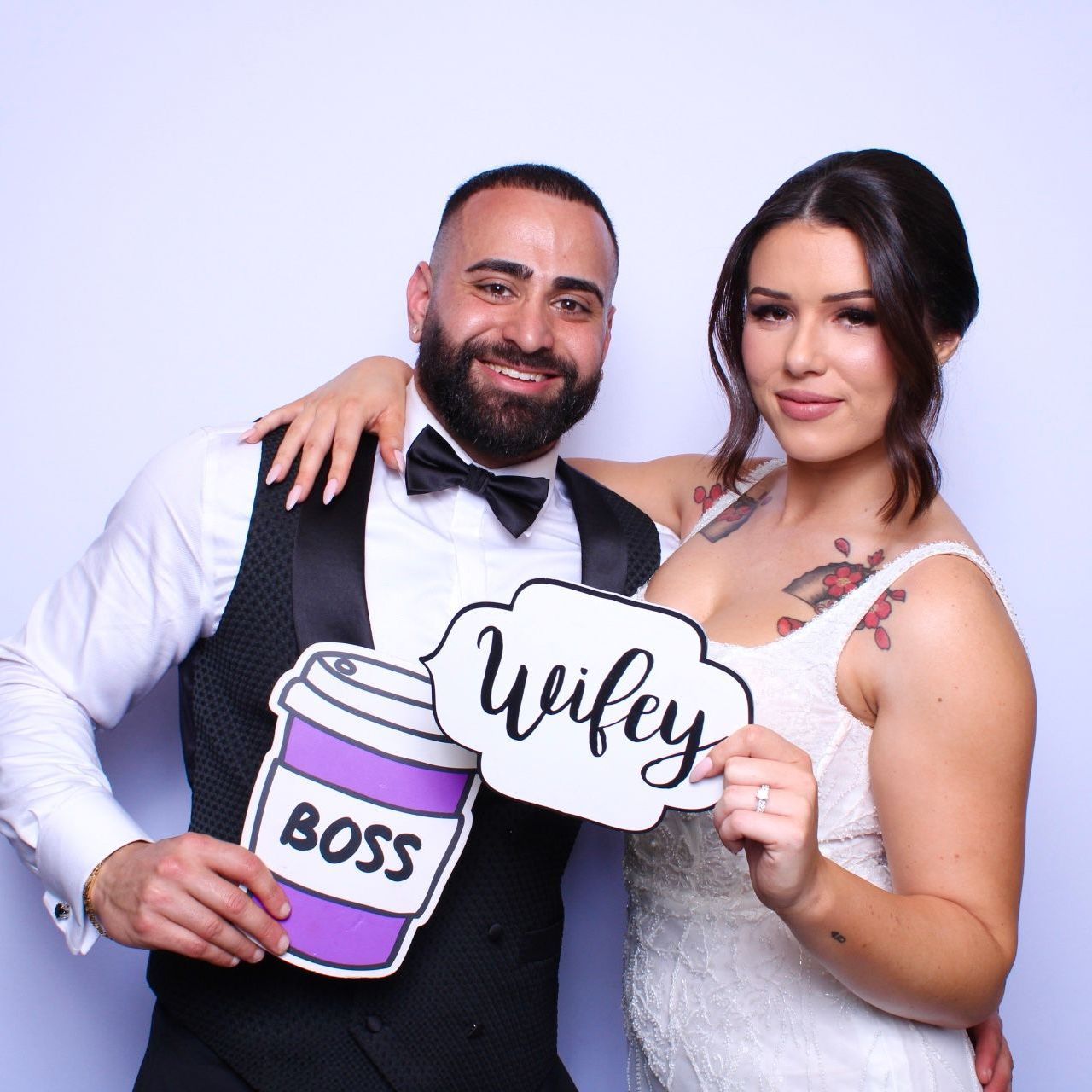 Couple in wedding attire posing for a photo, holding props that say 