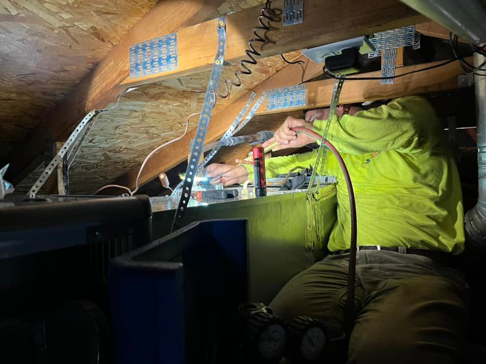 A man is working under a ceiling in an attic.