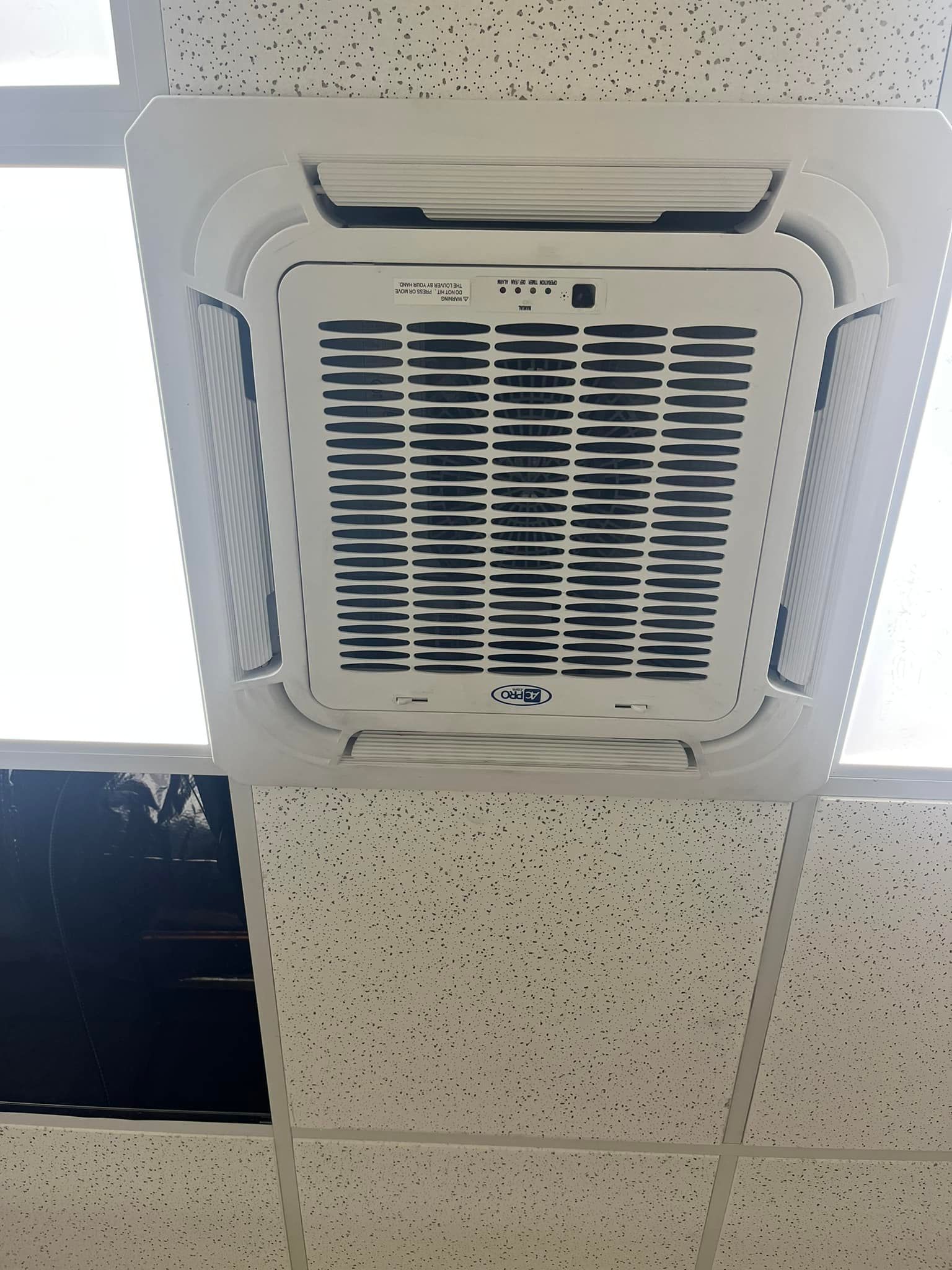 A white air conditioner is mounted to a tiled ceiling