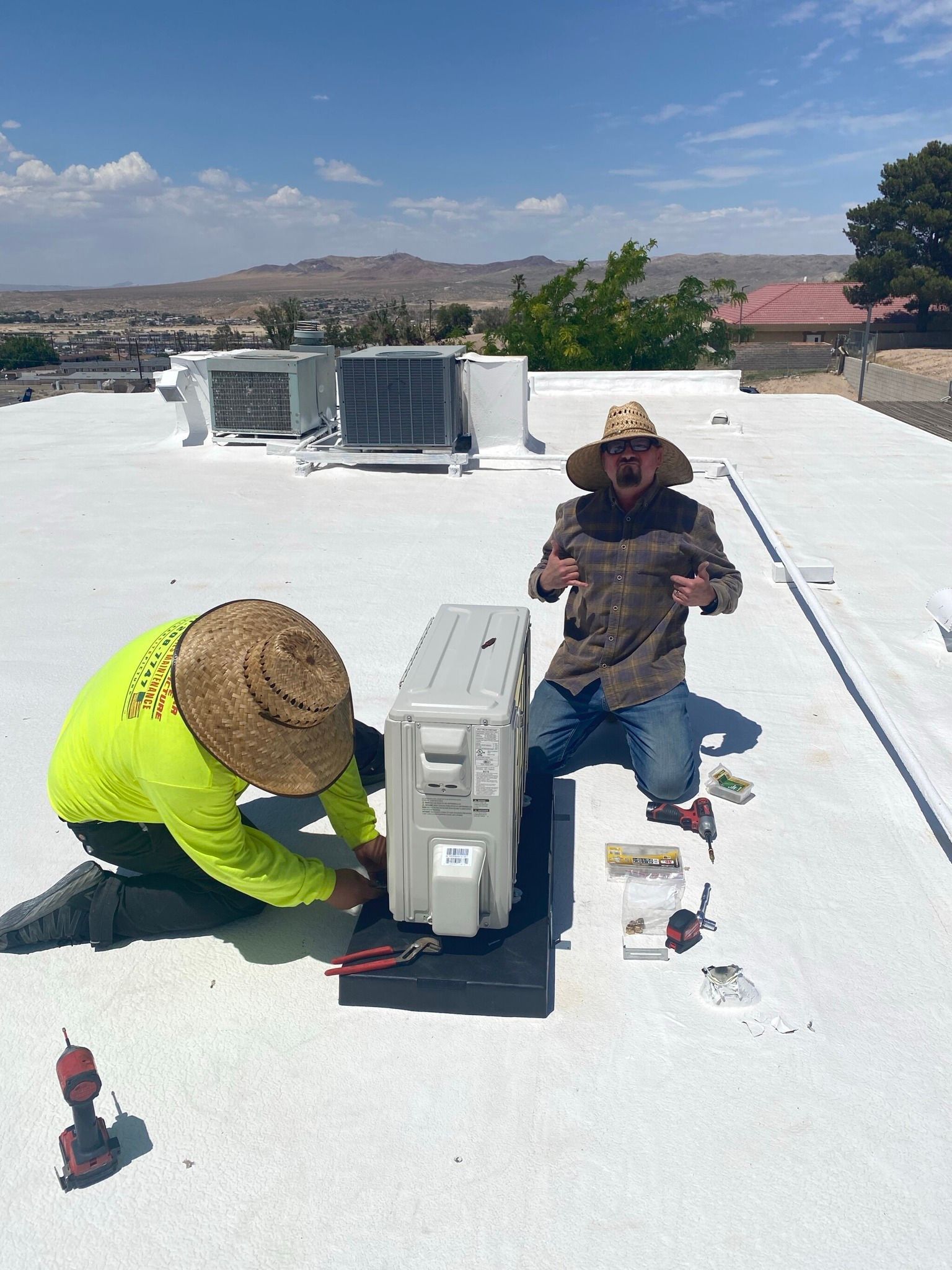 Two men are working on an air conditioner on a roof.