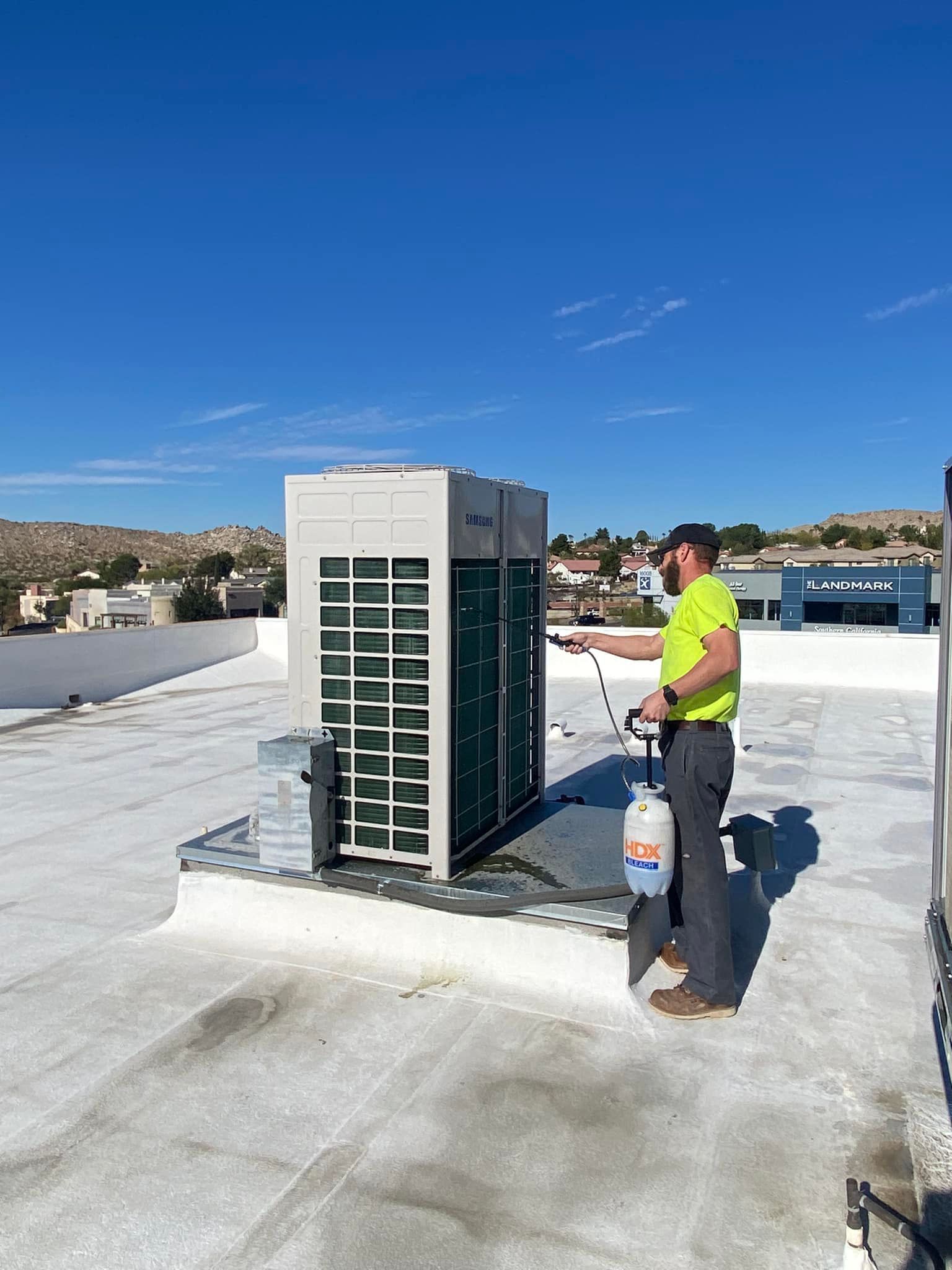 A man is spraying water on a rooftop air conditioner.