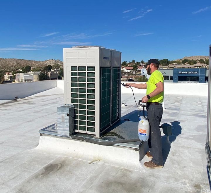 A man is spraying water on a rooftop air conditioner.