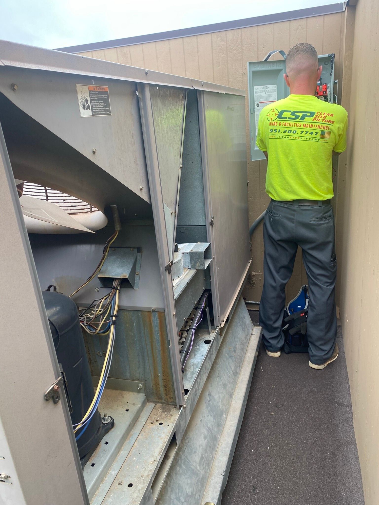 A man in a neon green shirt is working on an air conditioner.