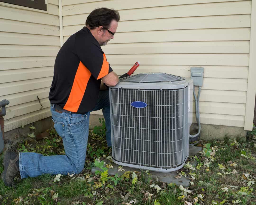 A man is working on an air conditioner outside of a house.