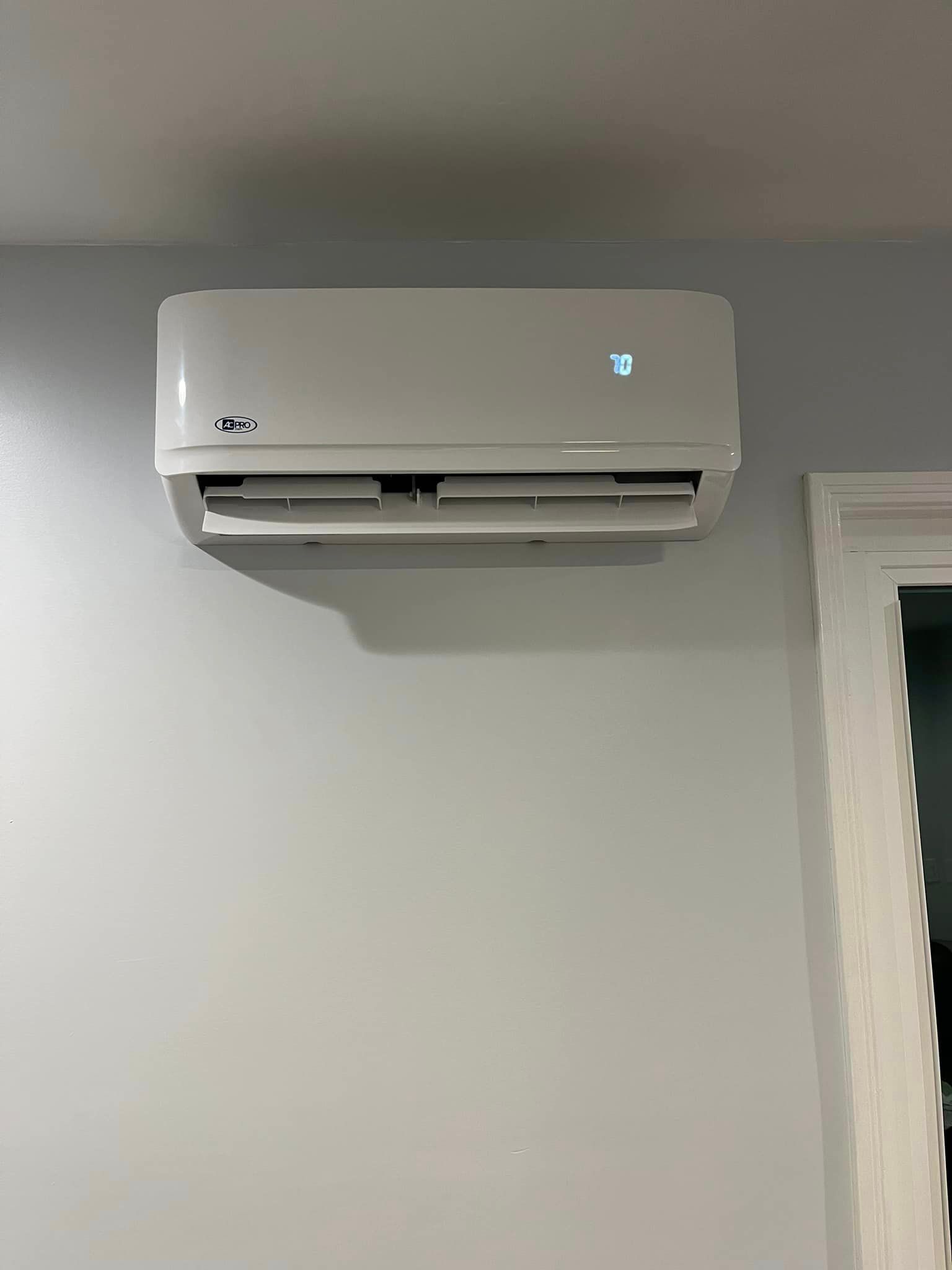 A white air conditioner is hanging on a white wall next to a window.