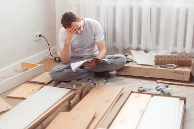 Person sitting on a floor among unpacked boards, holding papers and looking stressed during home renovation