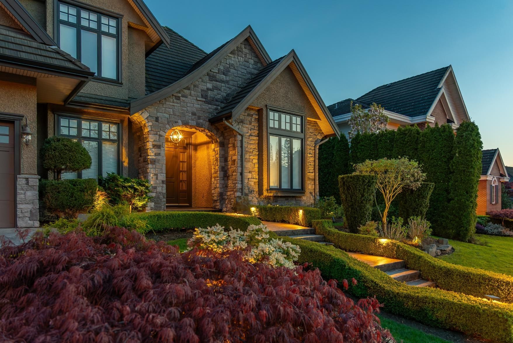 Luxurious house exterior at dusk with manicured landscaping and pathway lights.