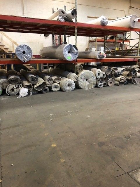 Warehouse storage of rolled carpet bolts on shelves and floor.