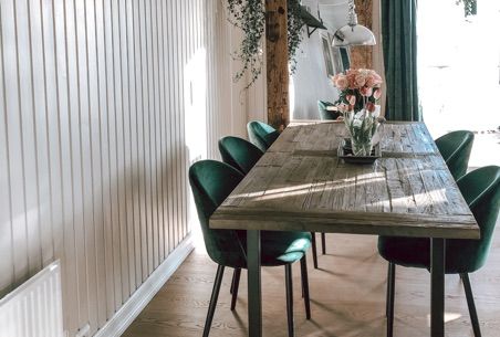 Dining room: Rustic wooden table with green velvet chairs, flowers, and vertical white panel walls.