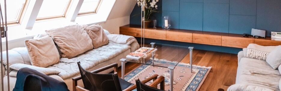 Cozy living room with blue wall and wooden floor. Two sofas with cushions, glass coffee table, rug.