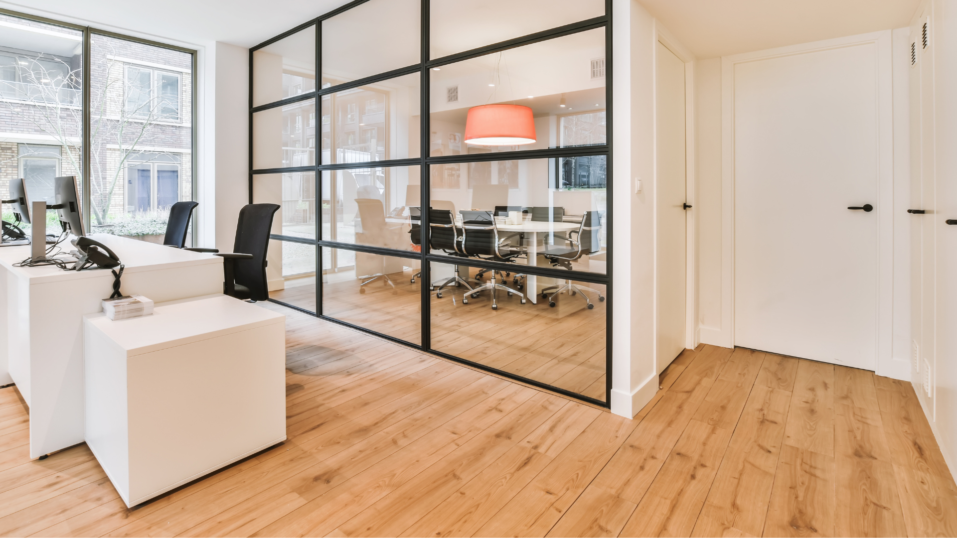 Office space with glass-walled conference room, white desks, wooden floors.