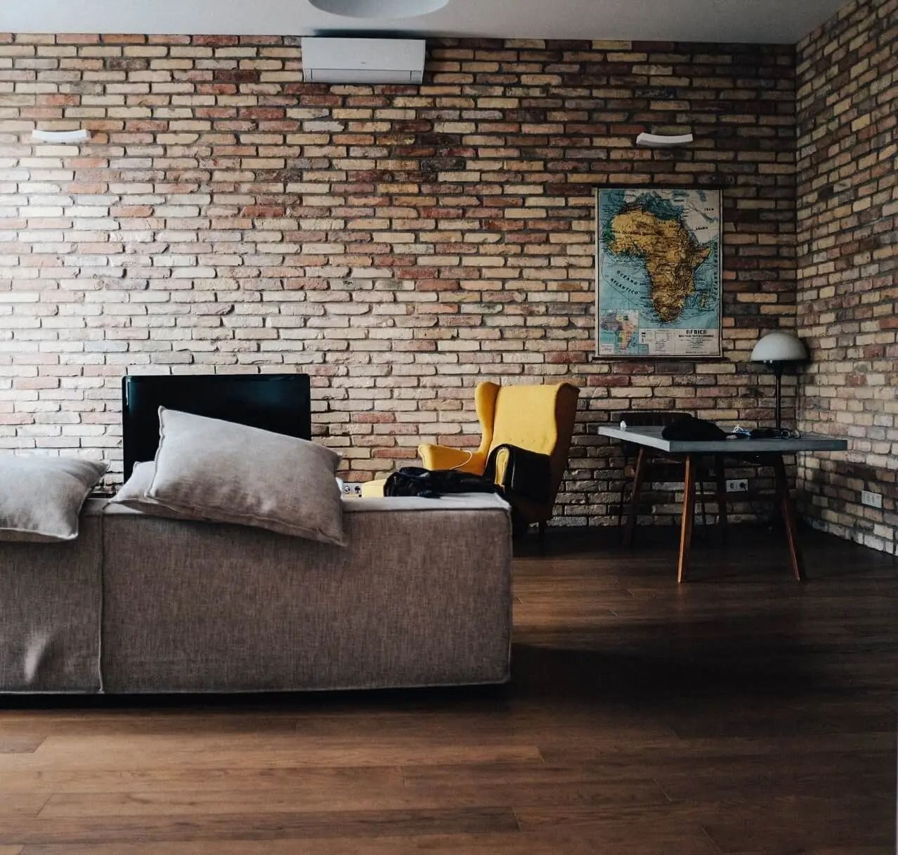 Living room with brick walls, sofa, yellow armchair, desk, and map of Africa.