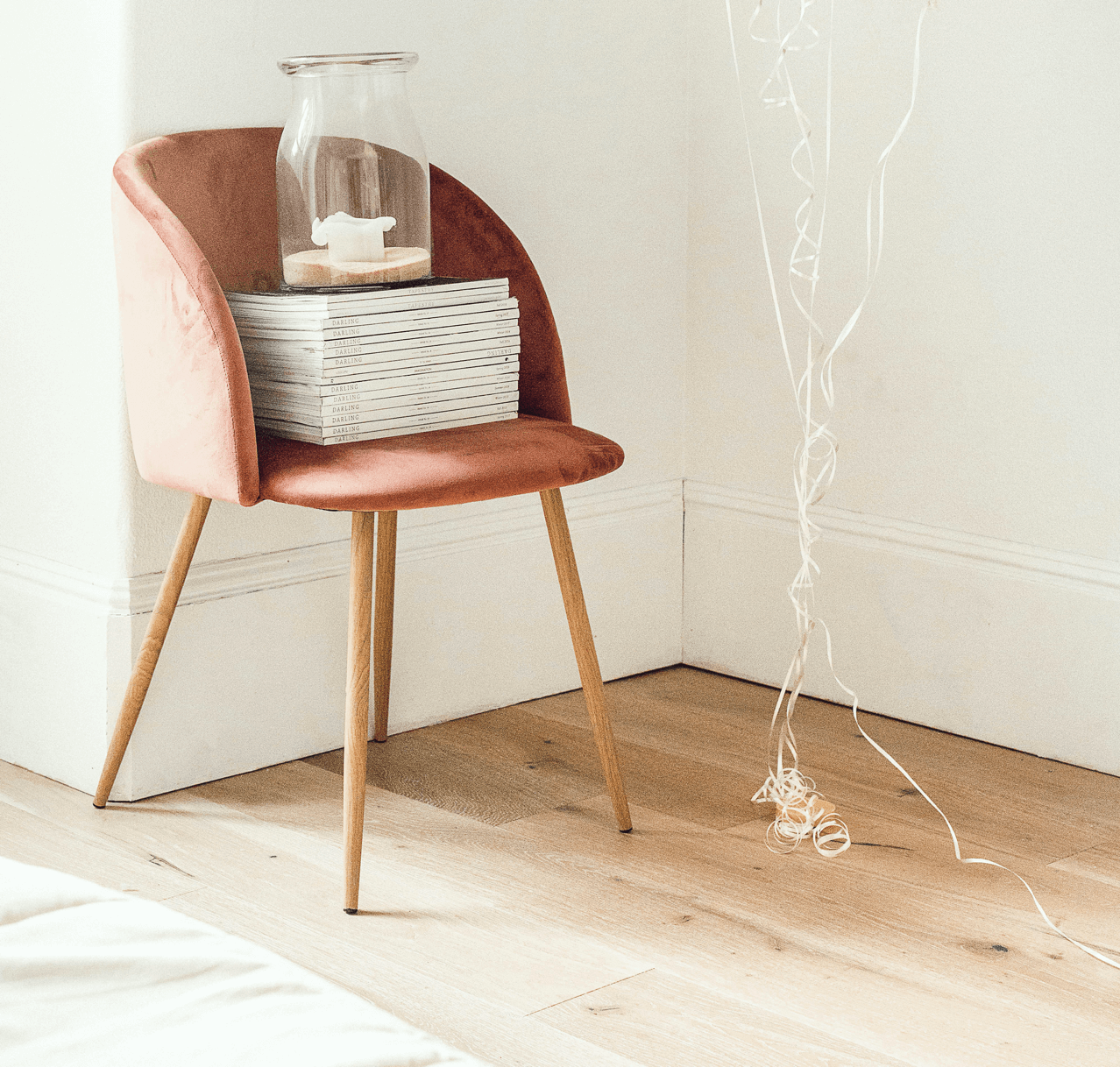 Pink chair with basket, jar, and decorative string in a white room.