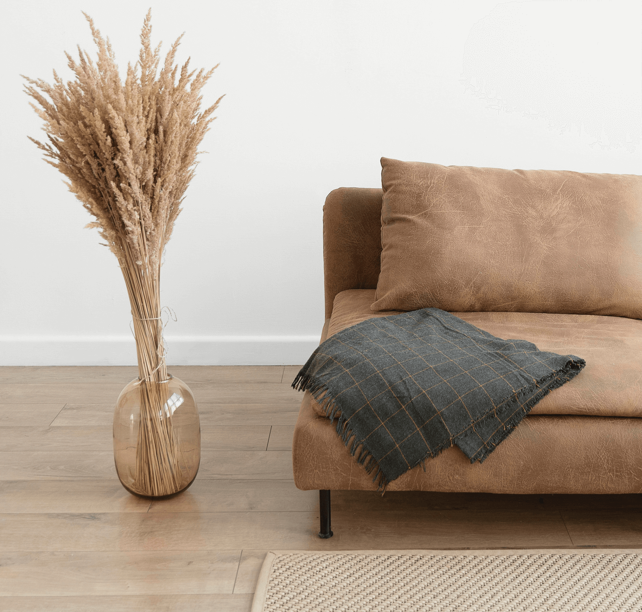 Brown couch with a gray throw blanket and a vase of dried plants.