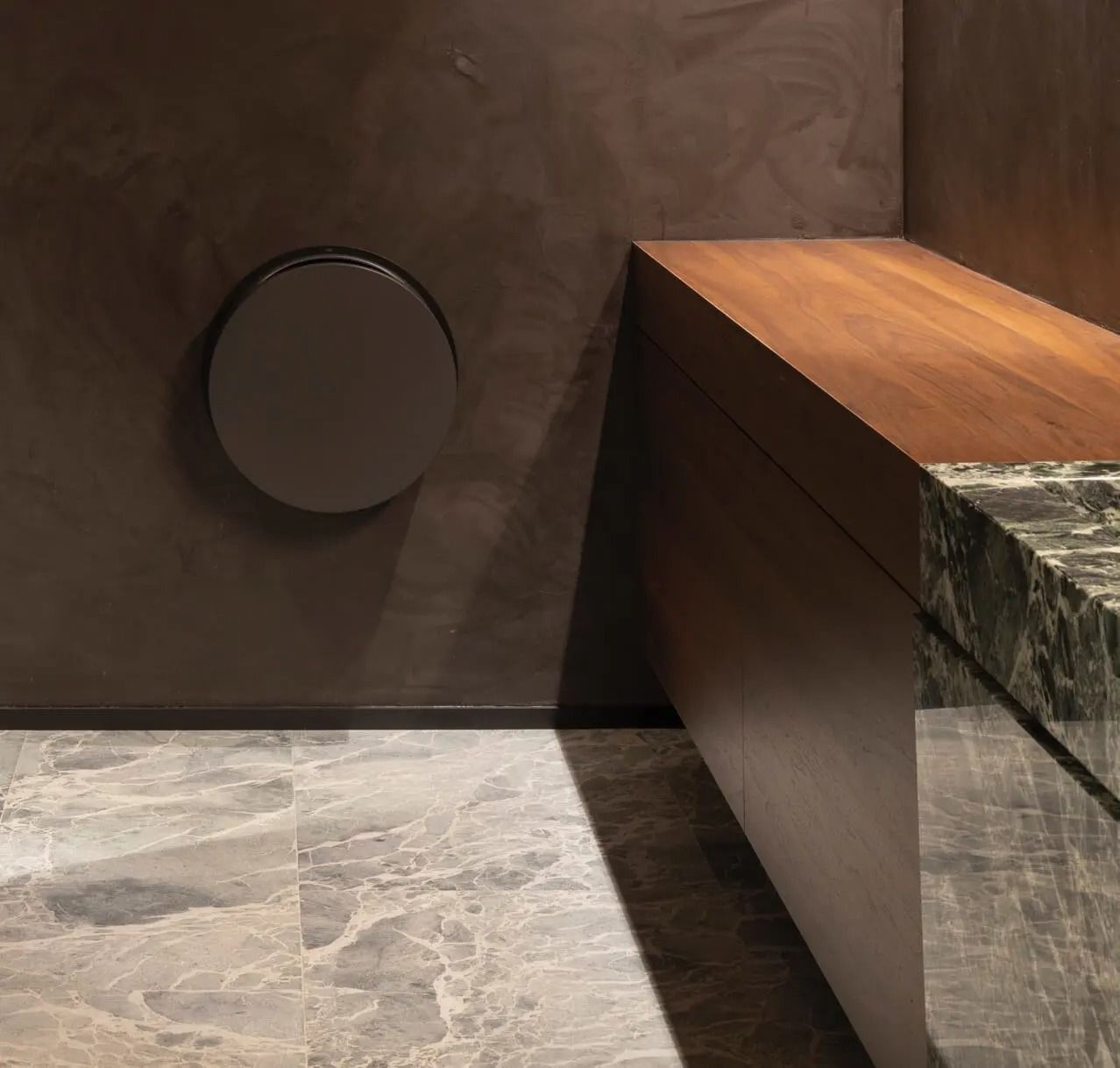 Dark bathroom corner with a wooden countertop, marble tiles, and a circular vent.
