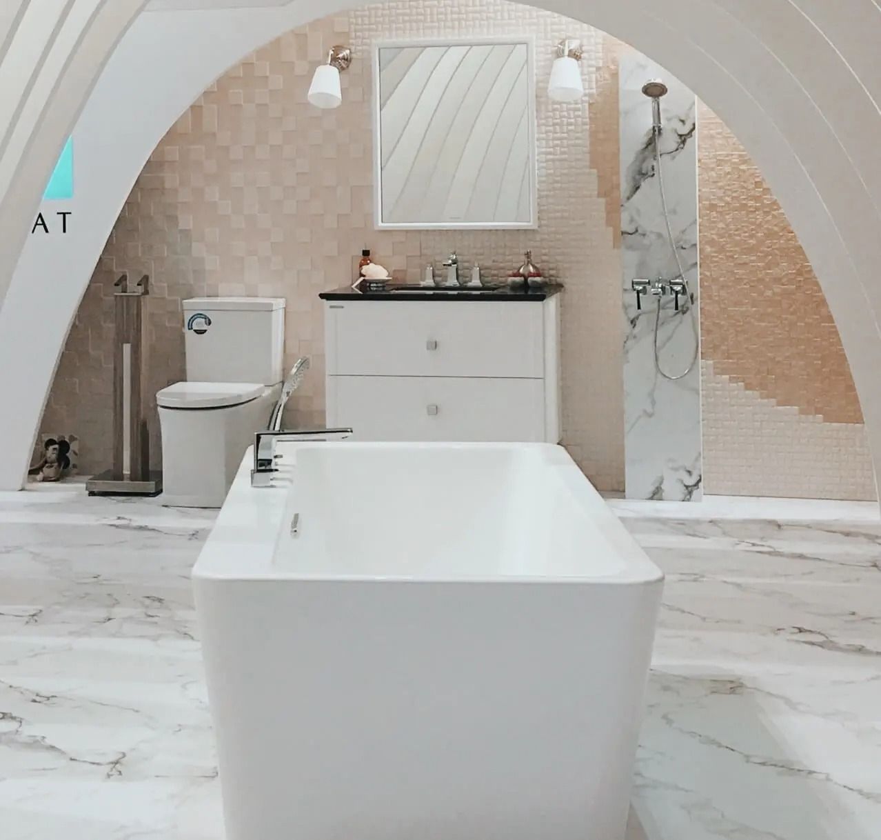 Modern bathroom with a white tub, toilet, and vanity against marble and patterned gold walls.