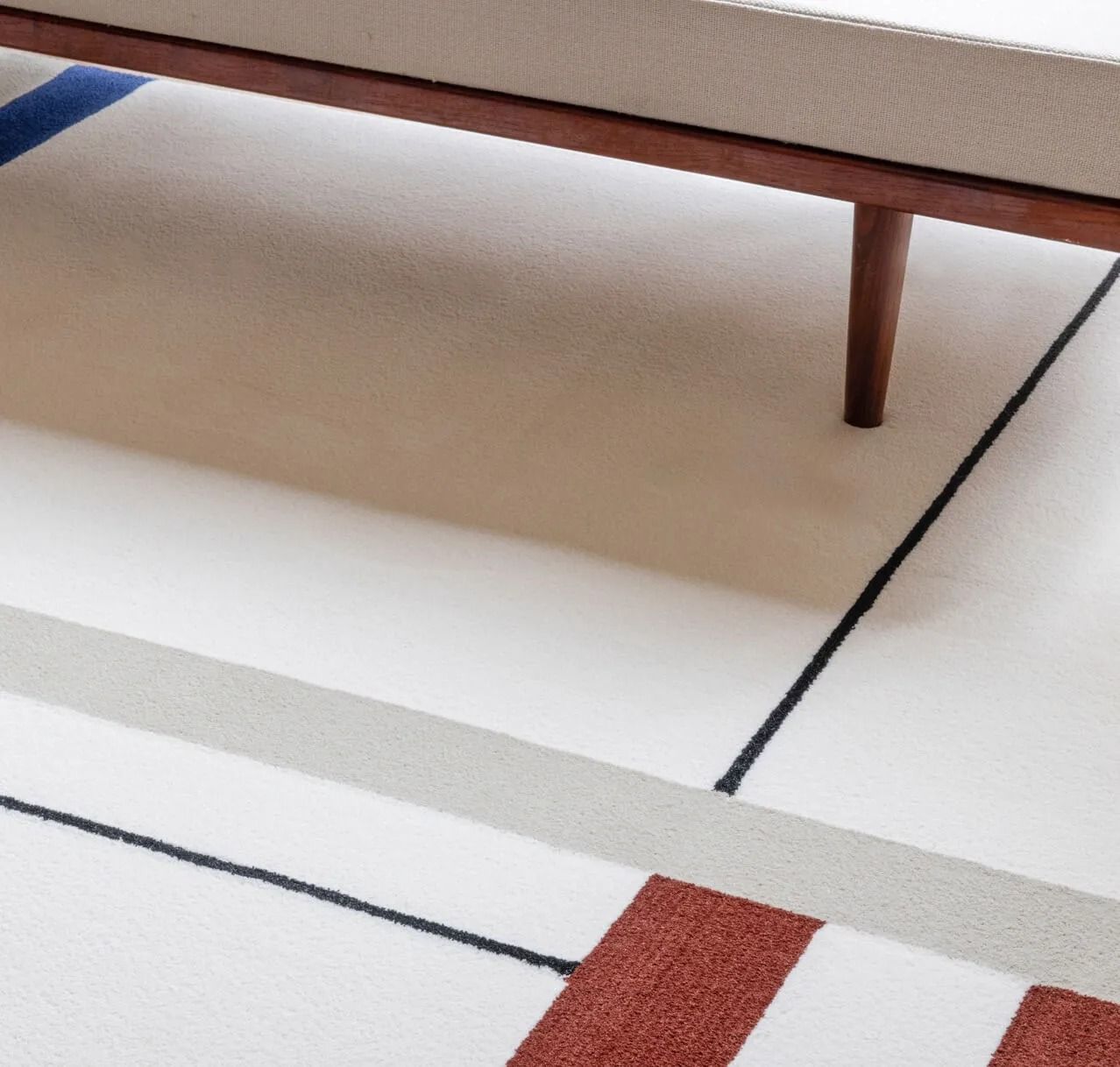 White rug with blue, red, and gray stripes and a wooden bench leg.