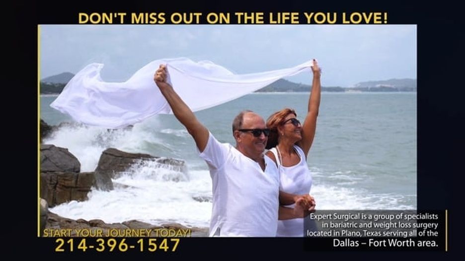 A man and a woman are standing on a beach holding a white cloth