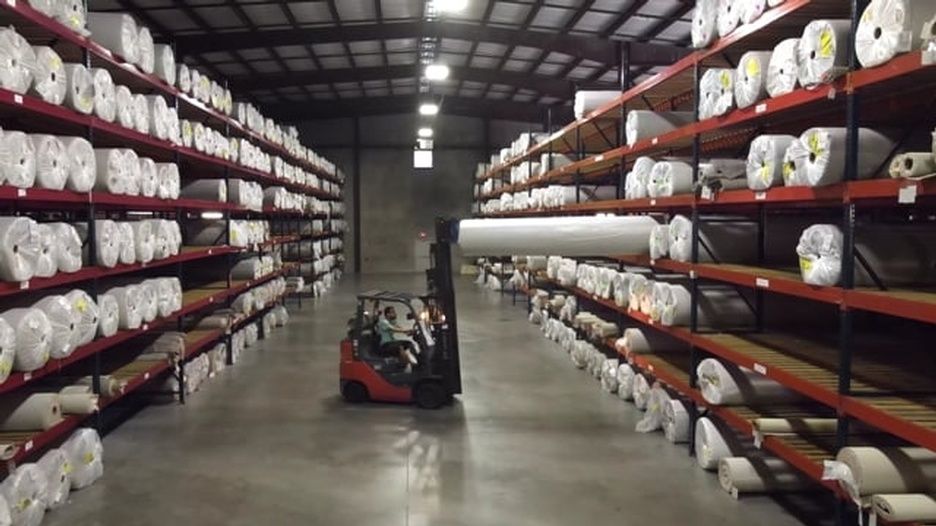 A forklift is driving down a warehouse filled with lots of shelves