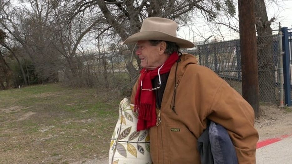 A man wearing a cowboy hat and scarf is holding a bag