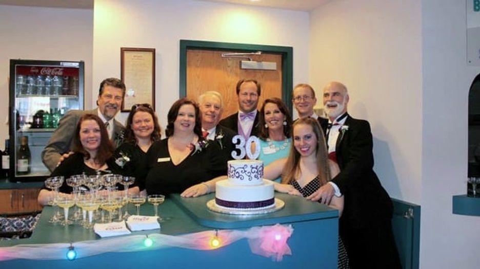 A group of people are posing for a picture in front of a cake with the number 30 on it
