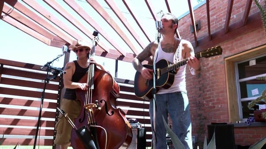 Two men are playing guitars and a double bass on a stage