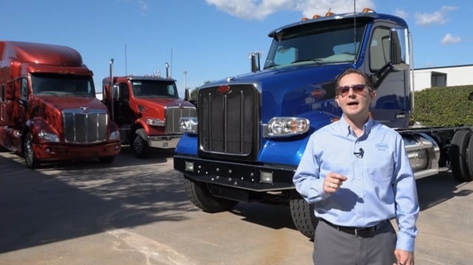 A man is standing in front of a row of semi-trucks