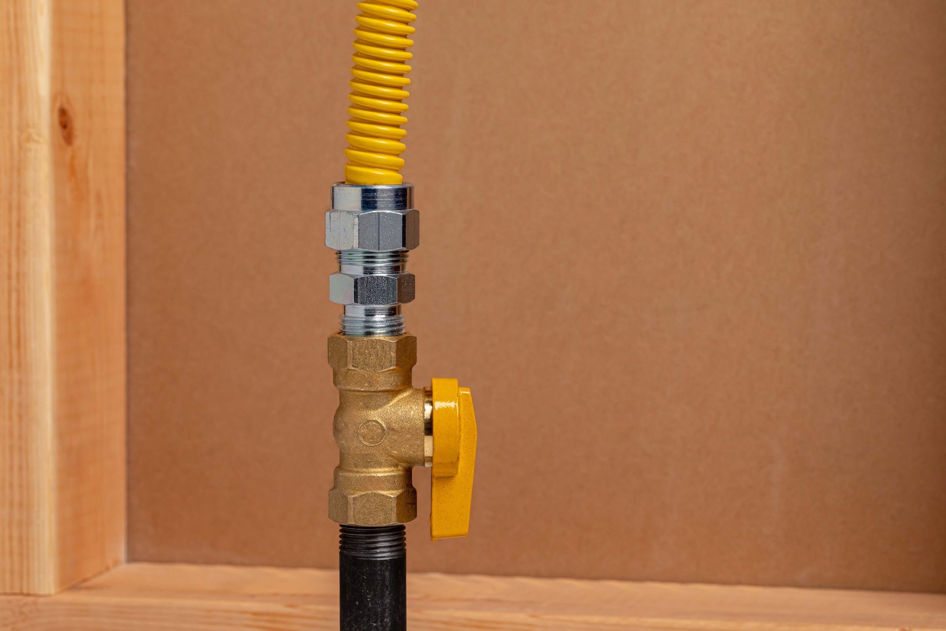 Yellow gas valve with a yellow flexible hose attached to a black pipe. Set against a brown background.