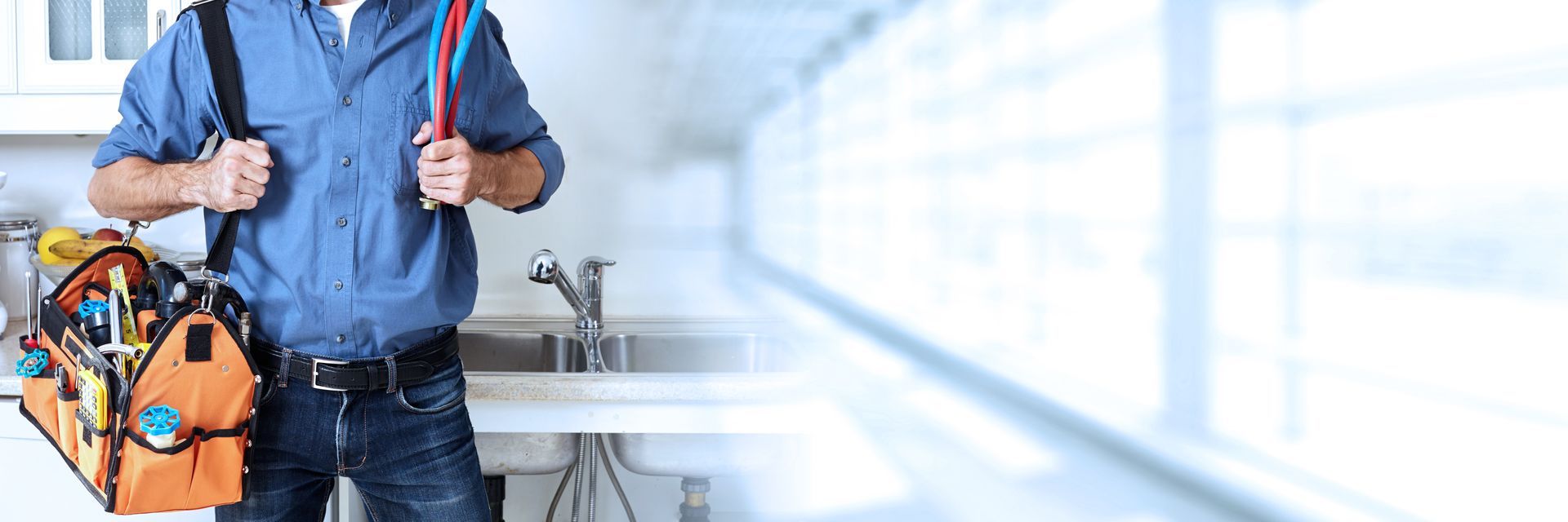 Plumber holding pipes with a tool bag beside a kitchen sink. Plumber holding pipes with a tool bag beside a kitchen sink.