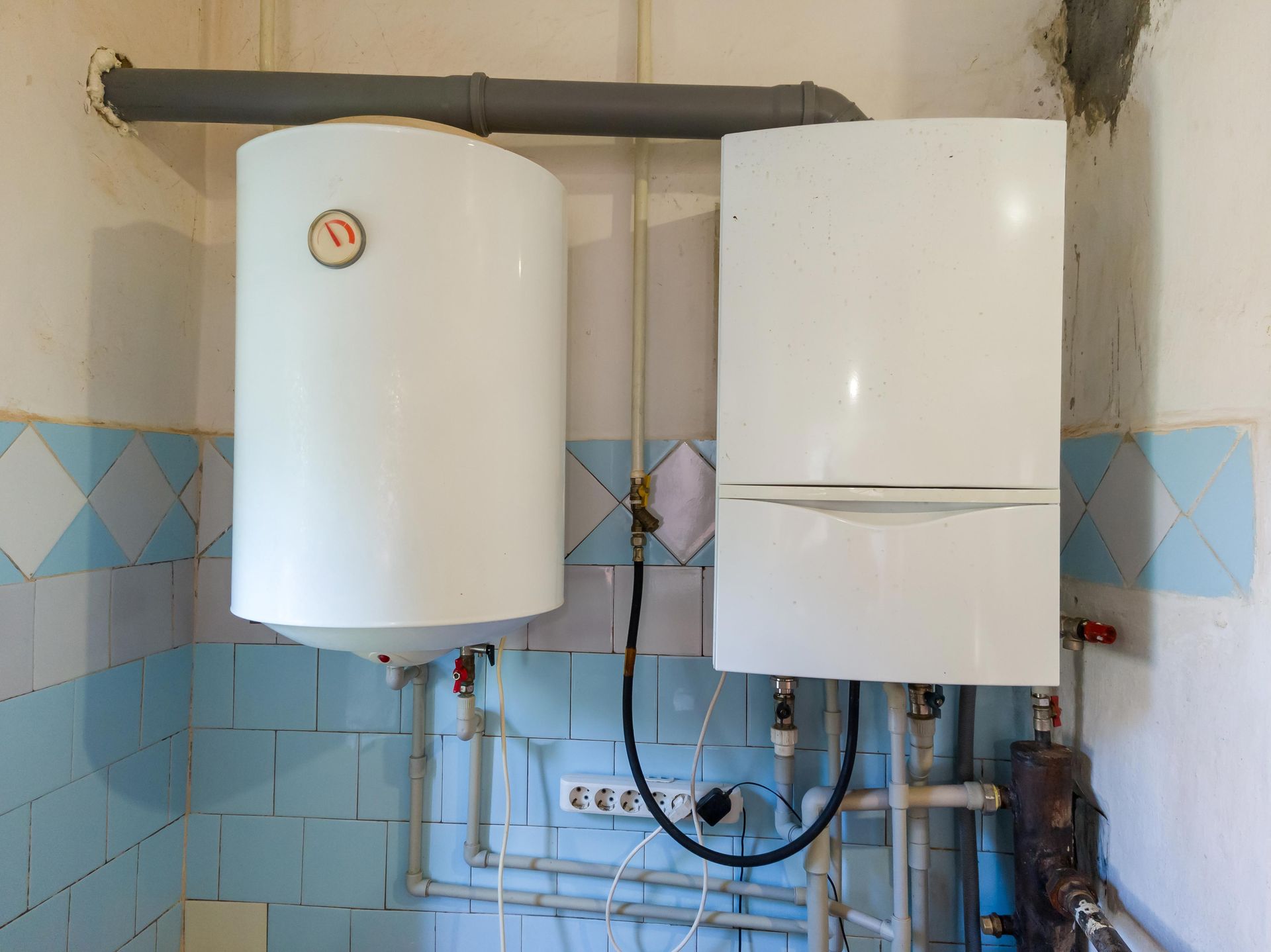 White water heater and boiler on a tiled wall, connected by pipes and wires.
