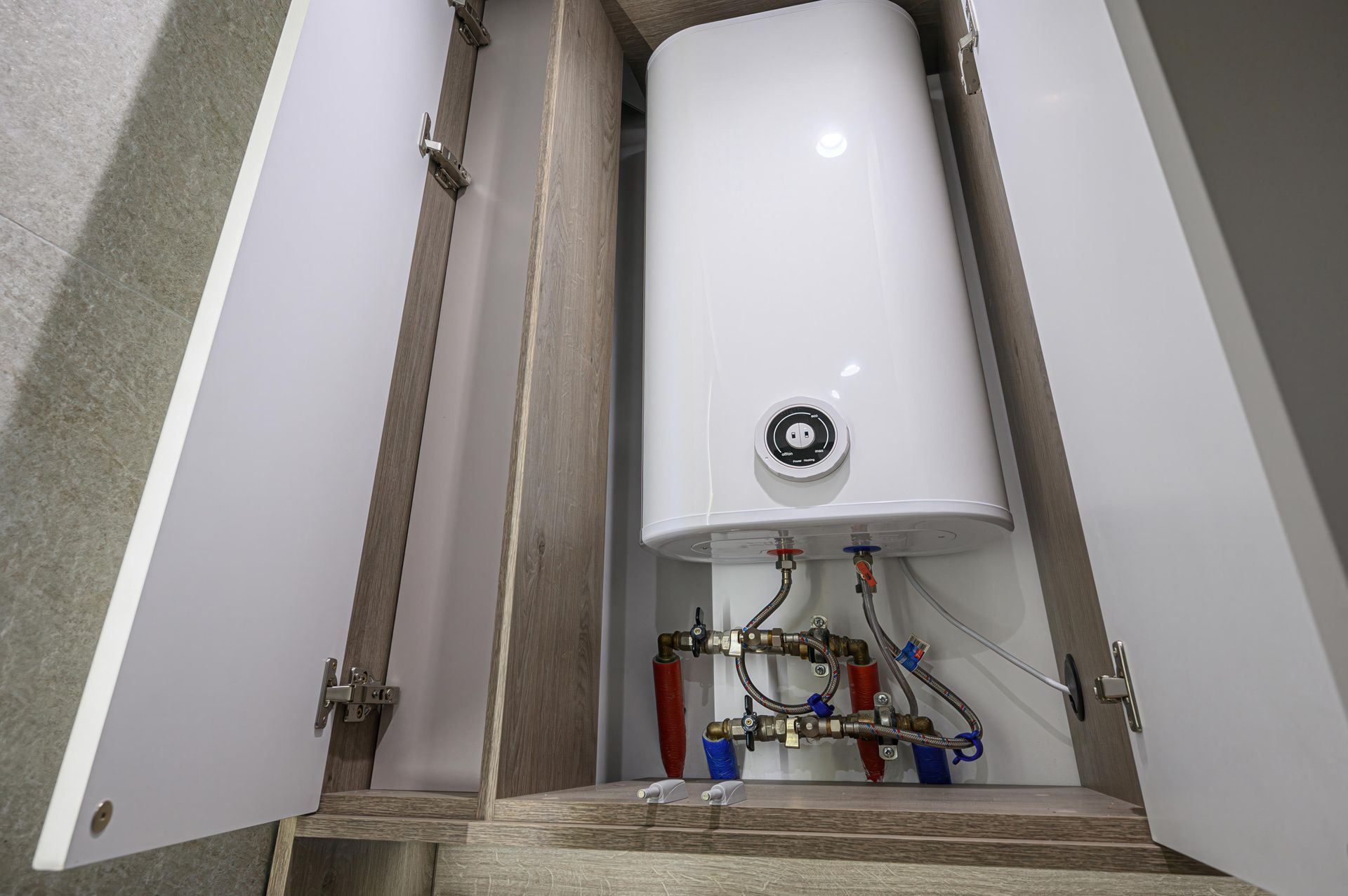 White water heater inside a cabinet with open doors, showing plumbing connections.