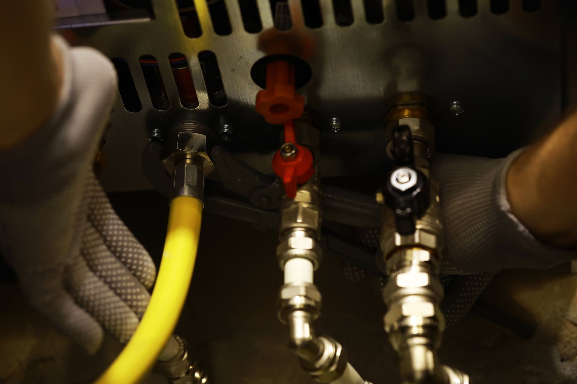Hands adjusting valves on a water heater. Yellow hose, red and black valve handles, silver pipes.