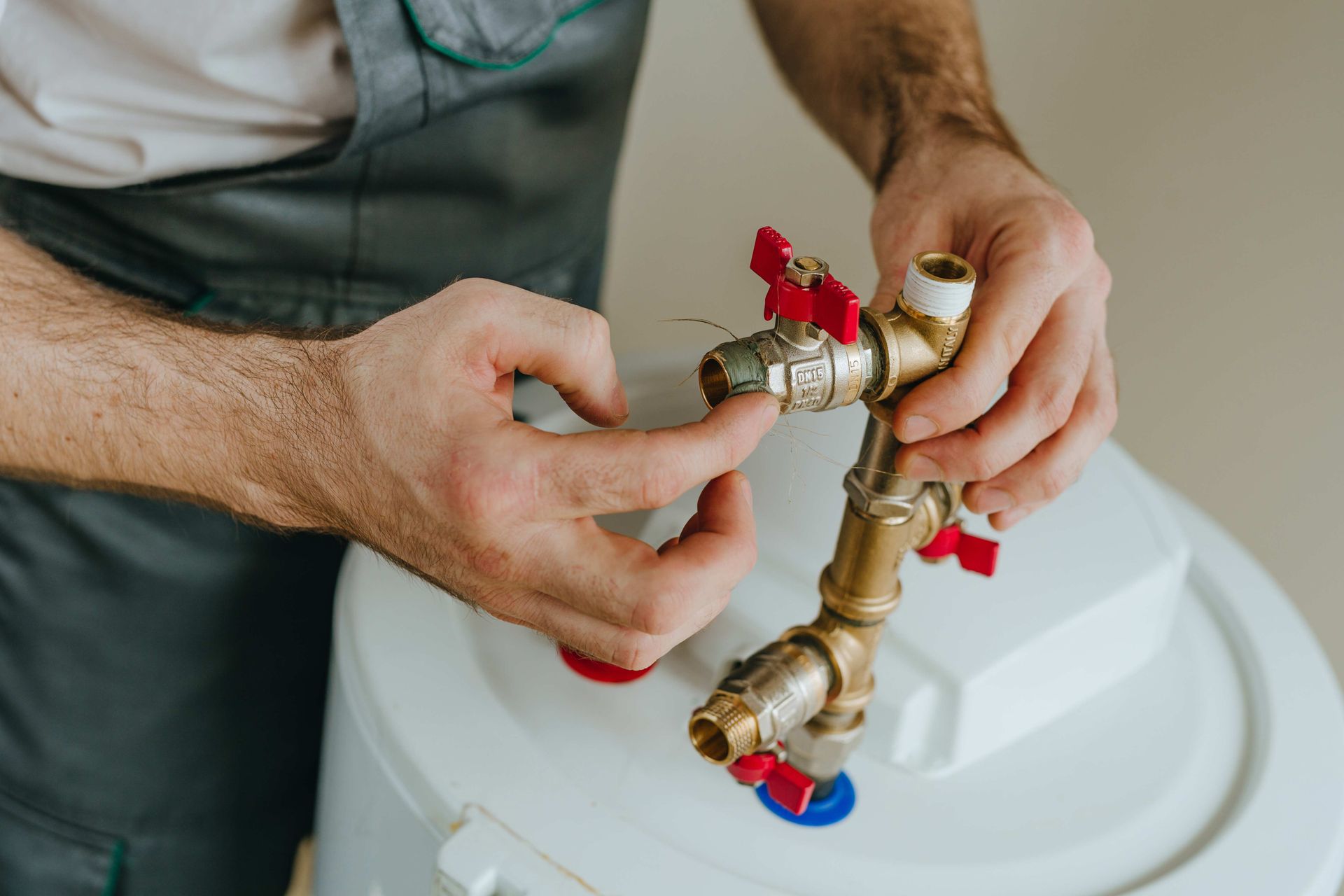 Plumber connecting pipes with red and blue valve handles to a water heater.