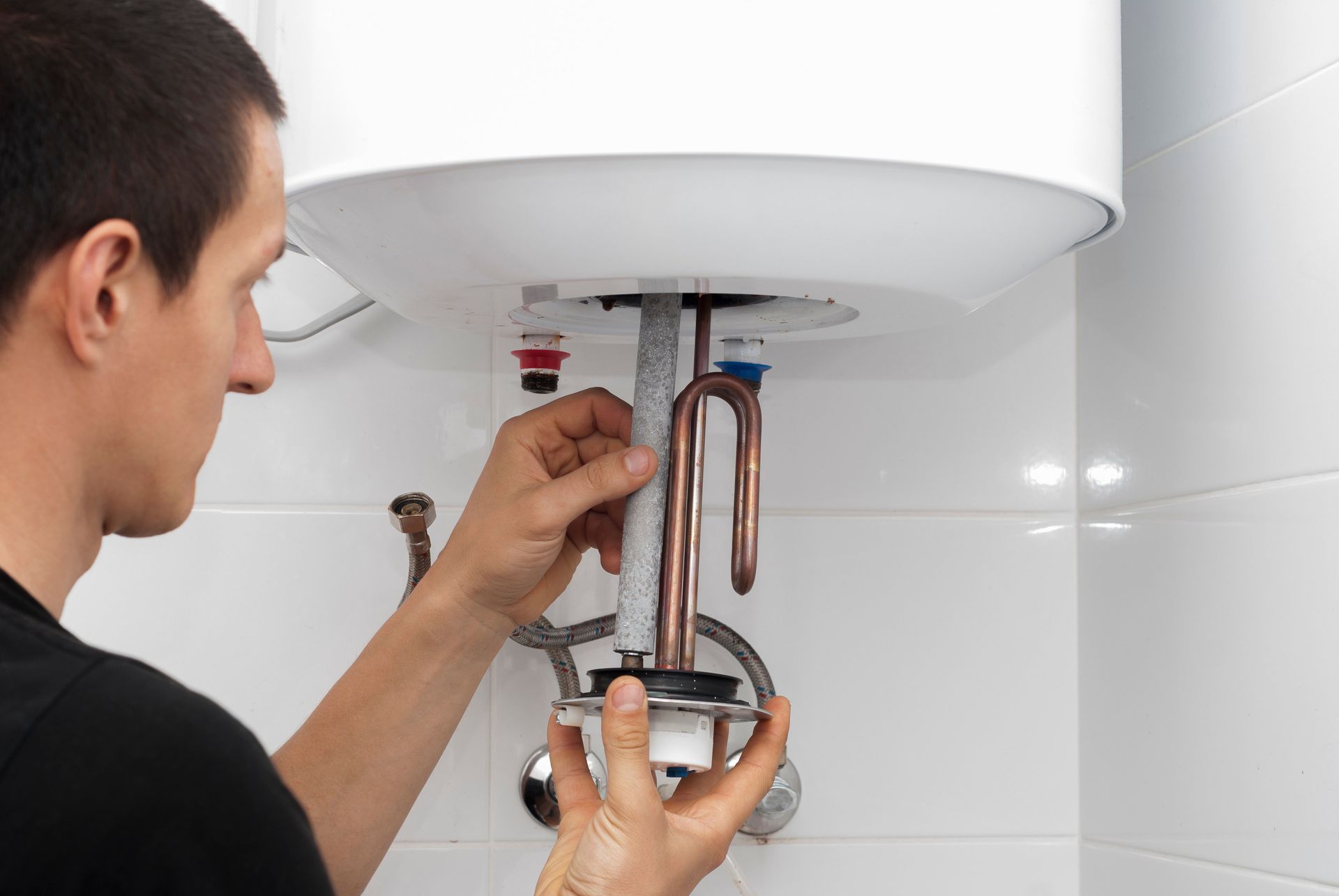 Man installing a water heater part. Copper pipes and water heater in a white tiled room.