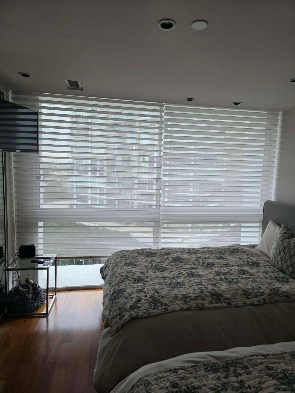 Bedroom with sheer white blinds over a window, bed with patterned comforter.