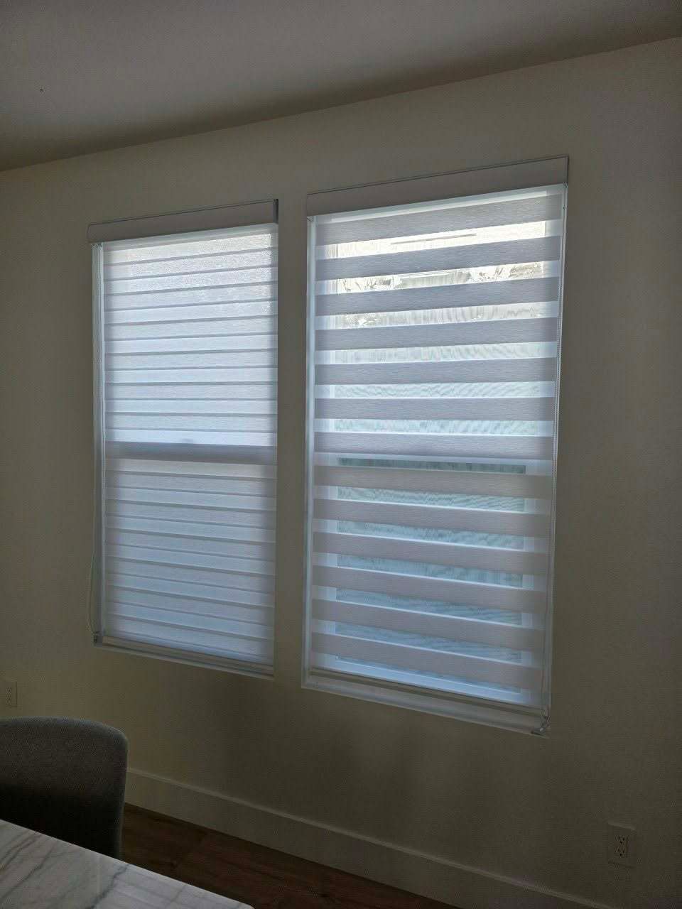 Two windows with white zebra shades in a room with light walls and wood trim.