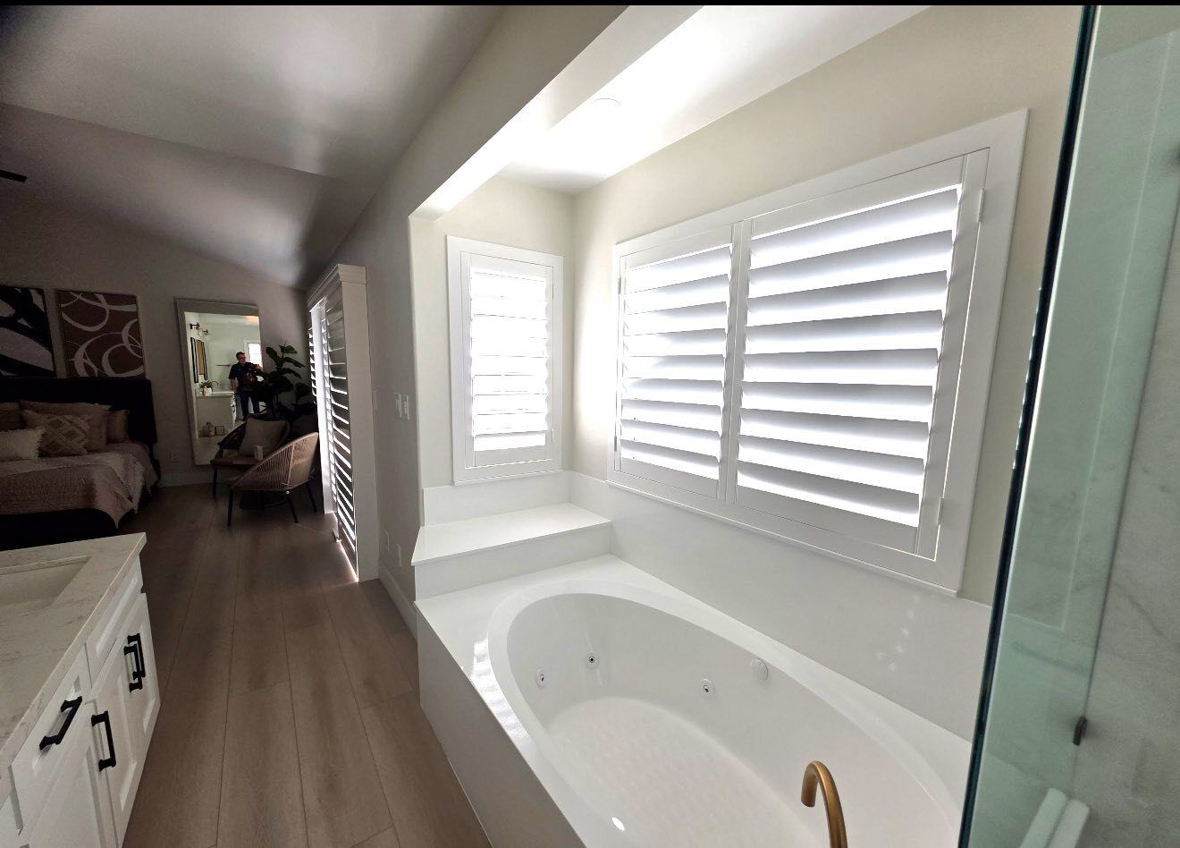 Bathroom with white shutters, a bathtub, and light-colored flooring.