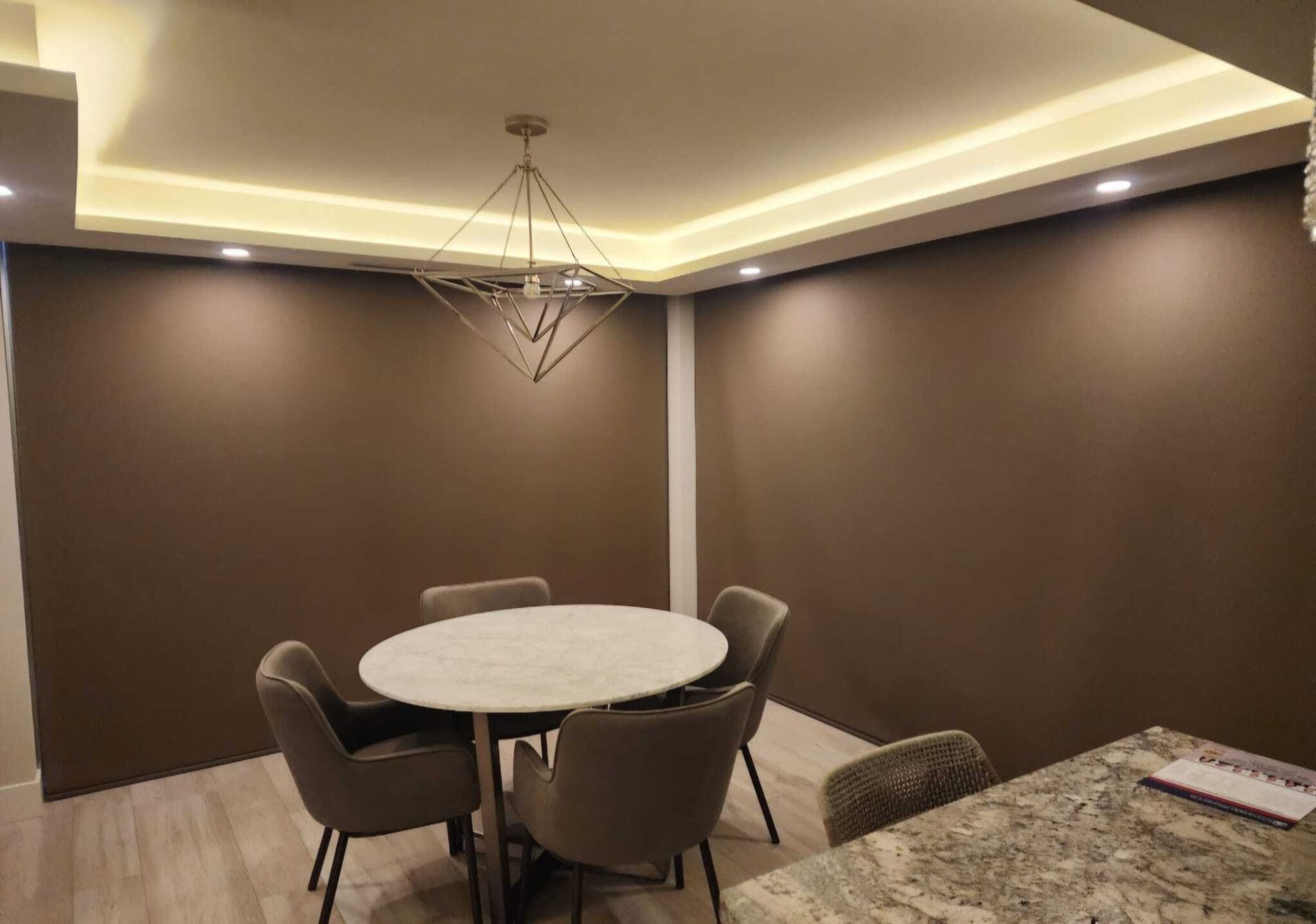 Dining room with round marble table, four gray chairs, brown walls, and geometric light fixture.
