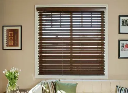 Brown wooden blinds on a window; a light-colored wall with framed pictures and a sofa below.