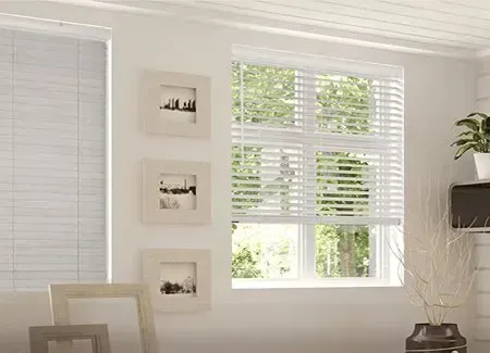 Bright white room with windows covered by white blinds, framed art, and decorative vase.