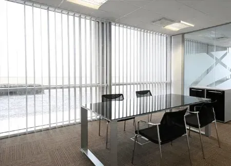 Modern office conference room with a glass table, black chairs, and vertical blinds.